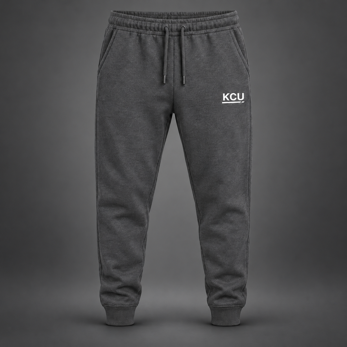 Charcoal men's joggers with a white KCU monogram on the left upper thigh and cuffed ankles.